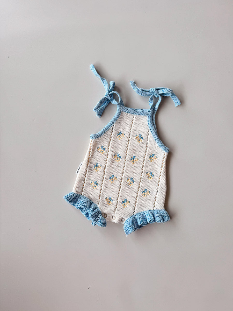Baby romper with floral pattern and blue trim on a gray background