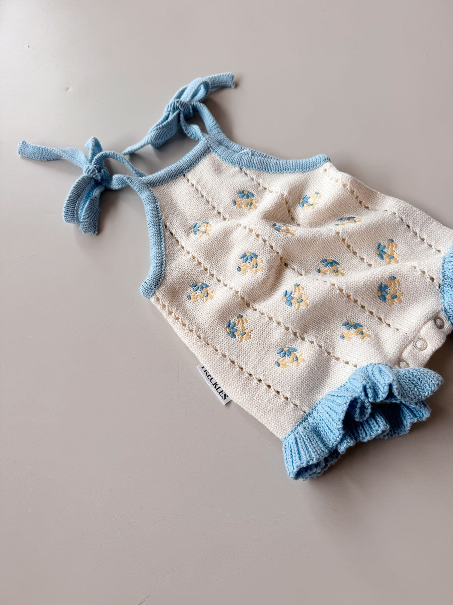 Baby romper with floral pattern and blue accents on a neutral background