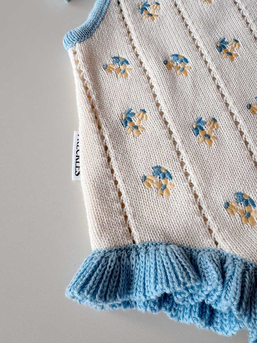 Knitted baby dress with blue trim and floral patterns on a plain background
