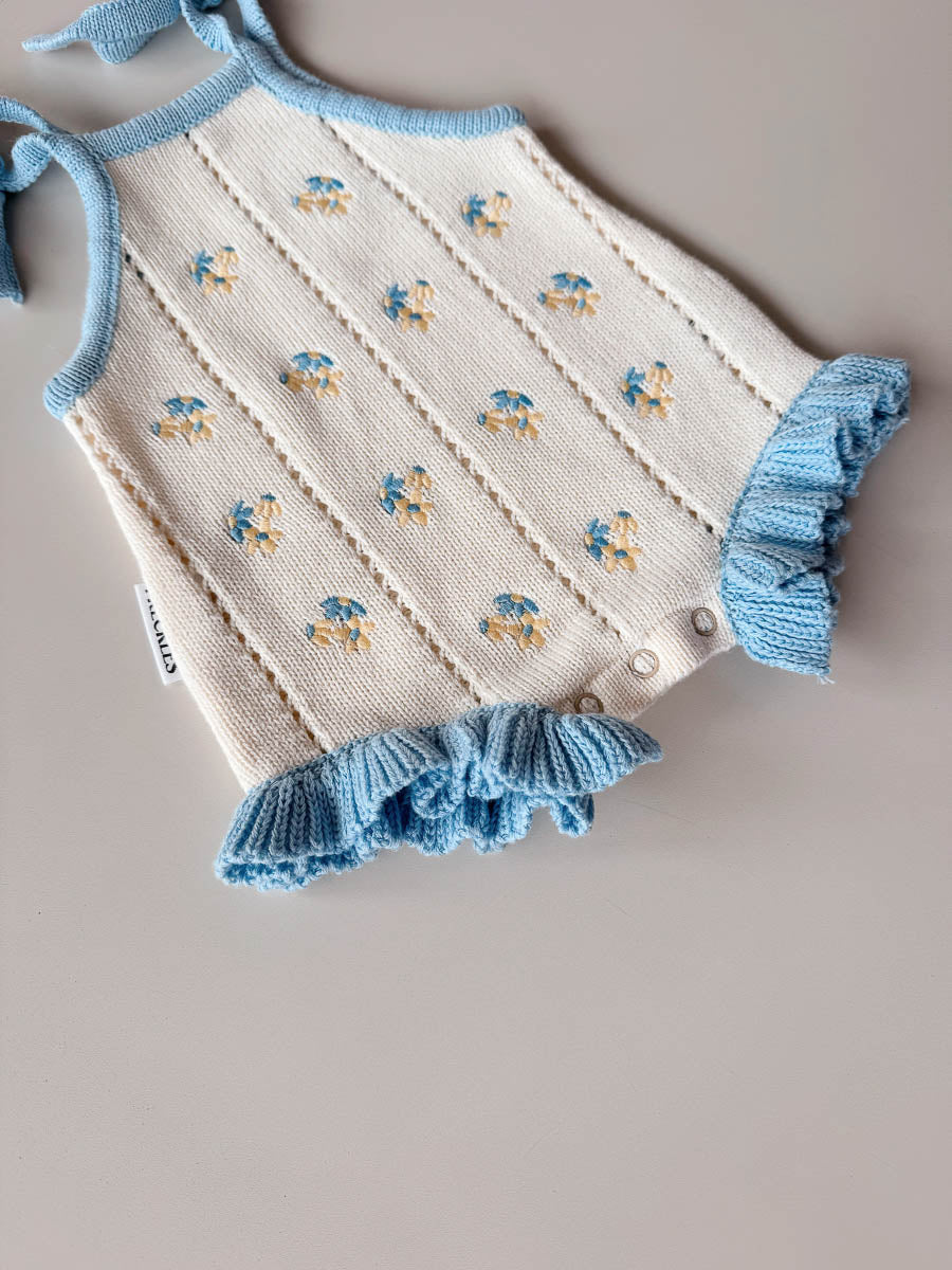 Baby romper with blue trim and embroidered design on a neutral background