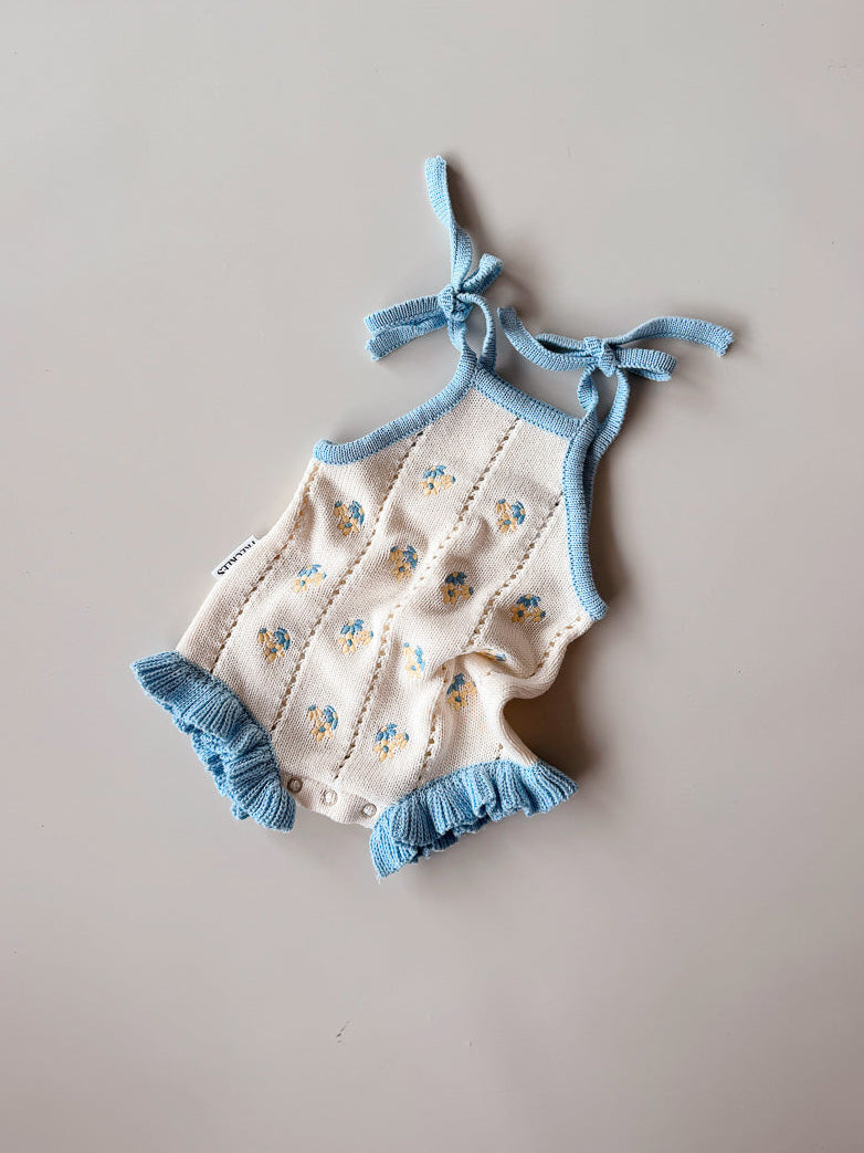 Baby romper with floral pattern and blue straps on a beige background