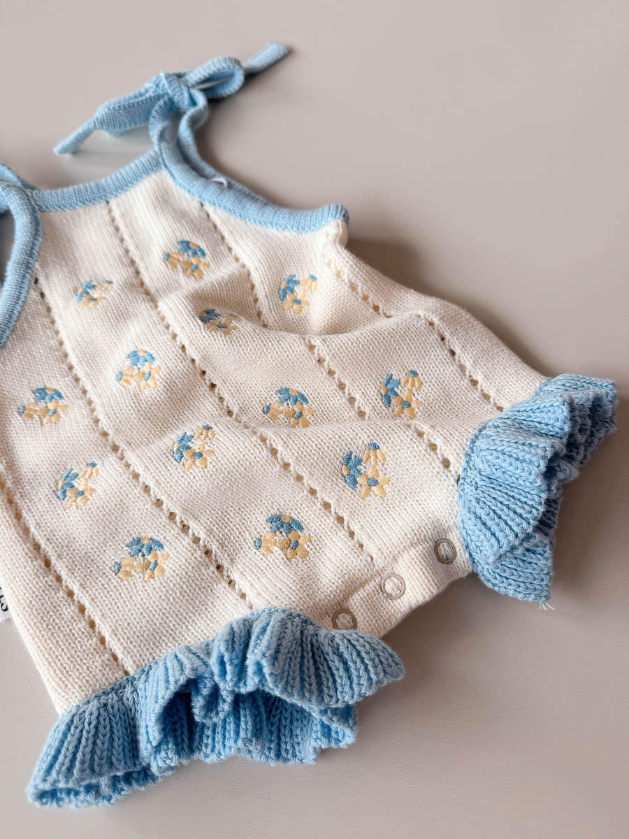 Knitted baby dress with blue trim and floral patterns on a neutral background
