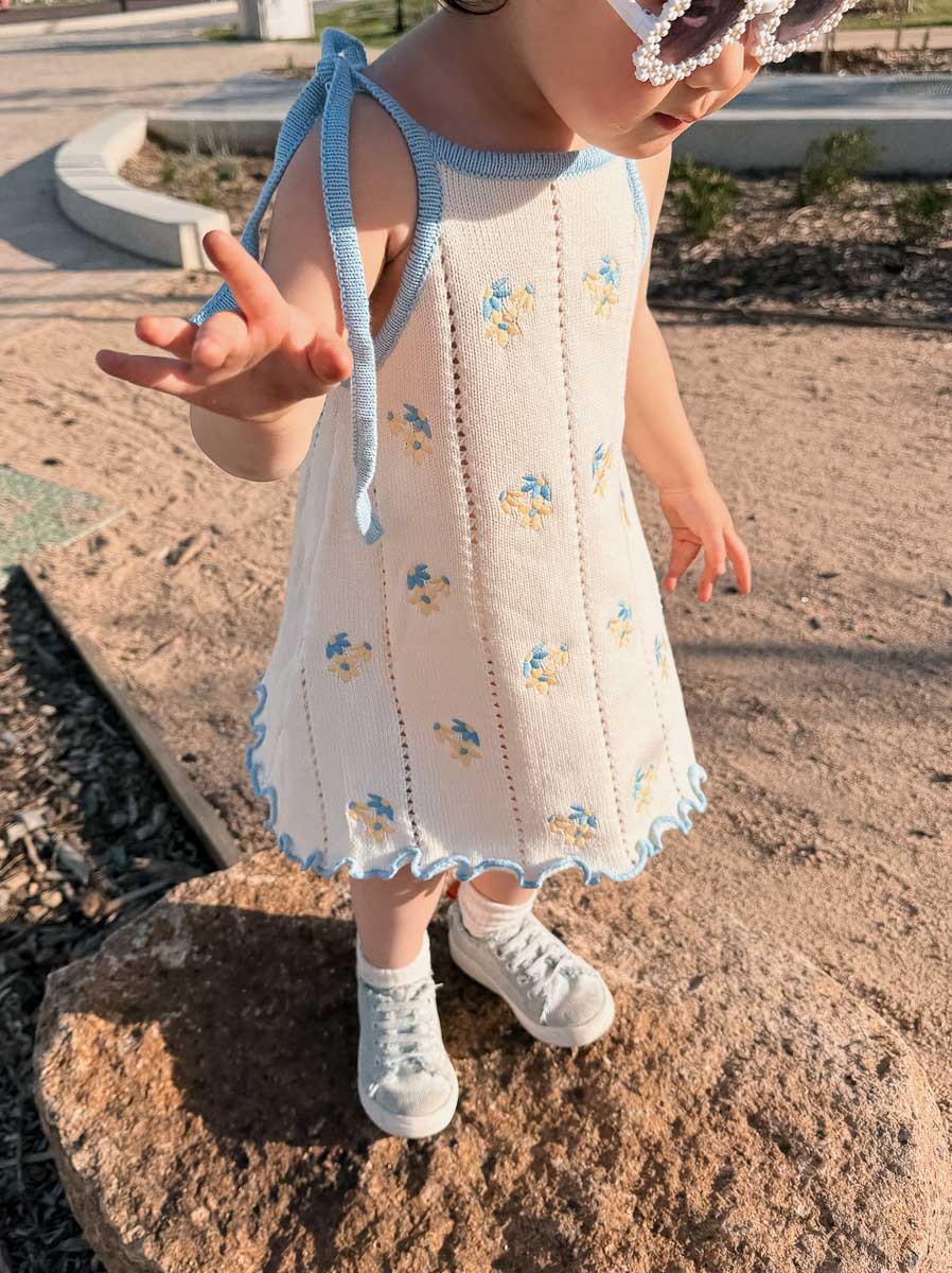 Child wearing a cream dress with blue yellow floral patterns on a stone surface.