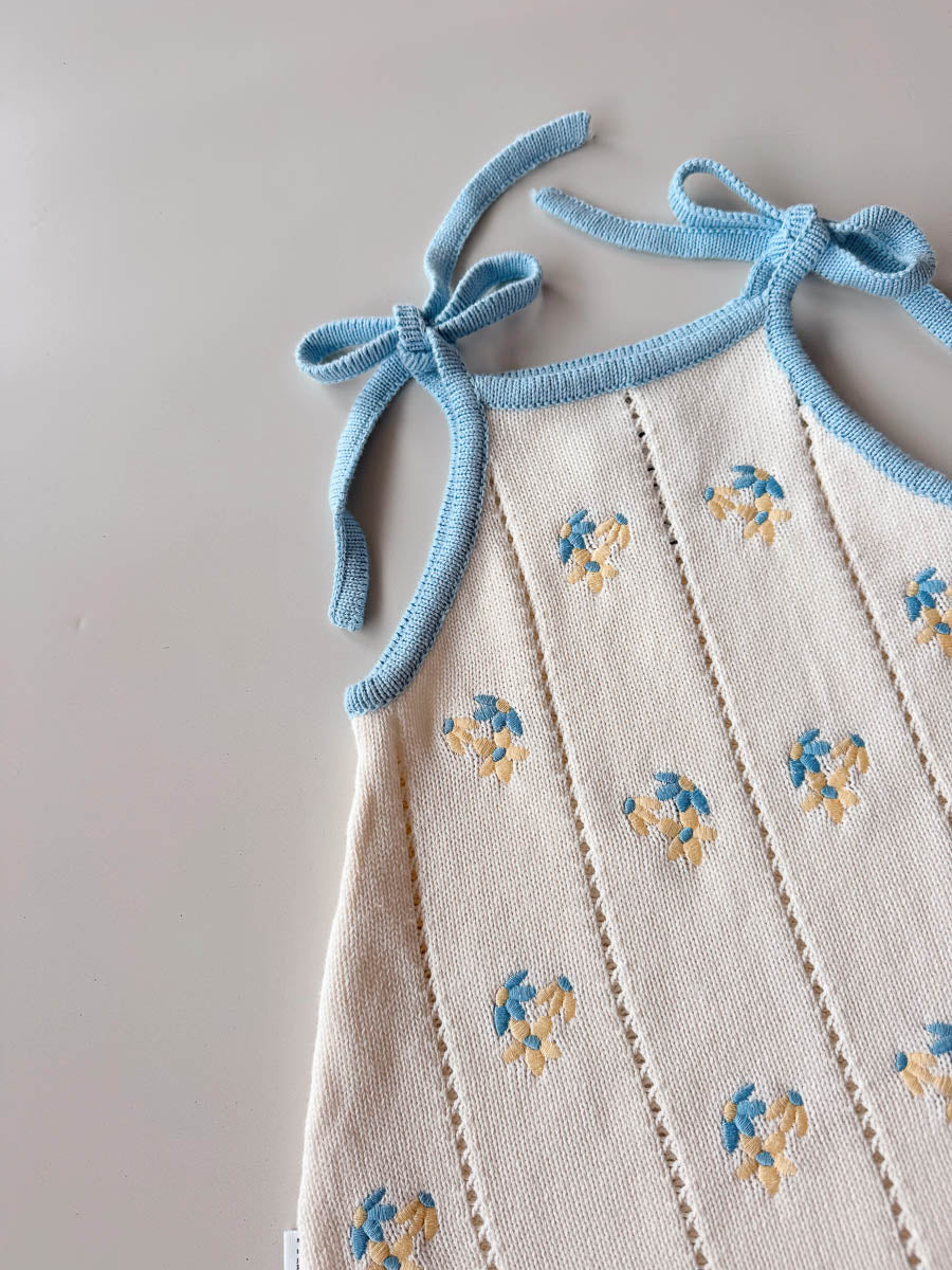 White dress with blue floral embroidery and blue straps on a light gray background