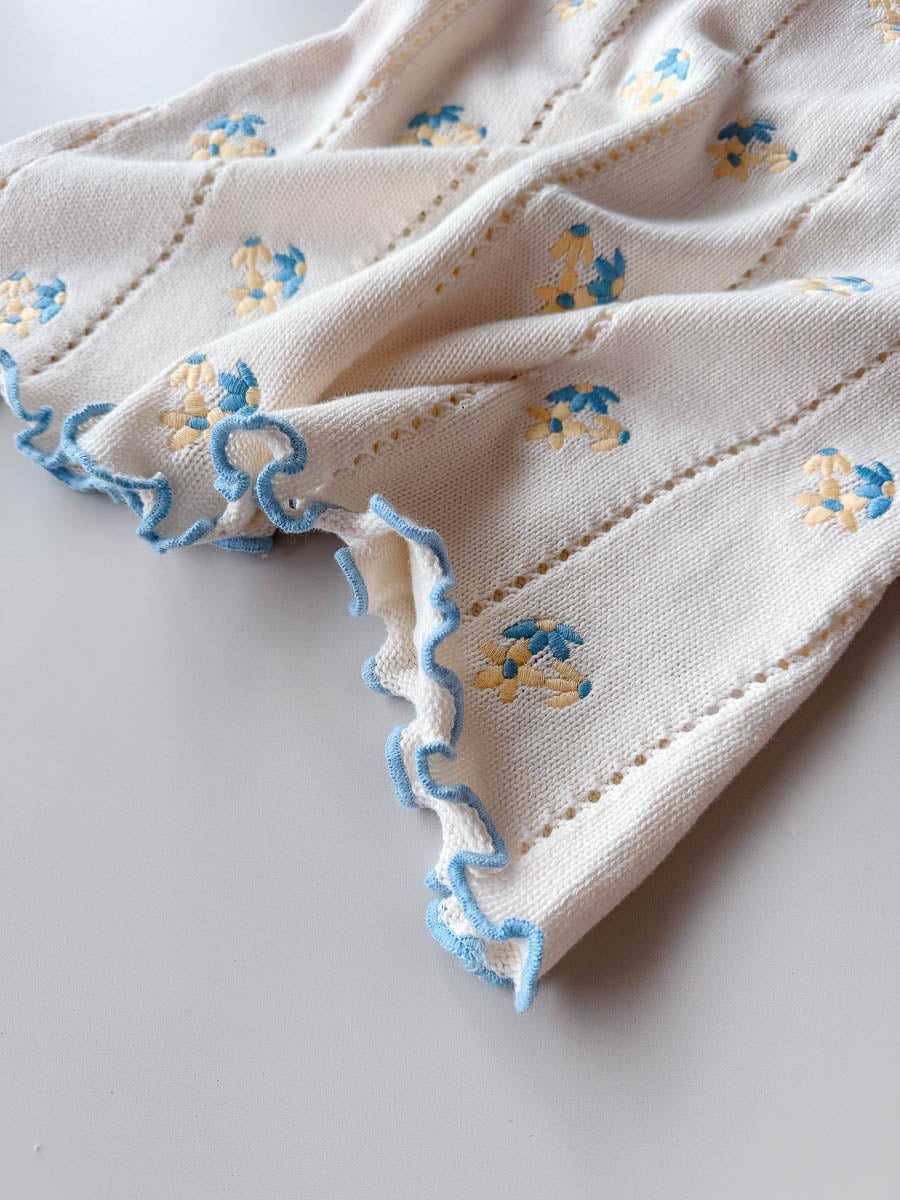 Close-up of a white fabric with blue floral embroidery on a light gray background